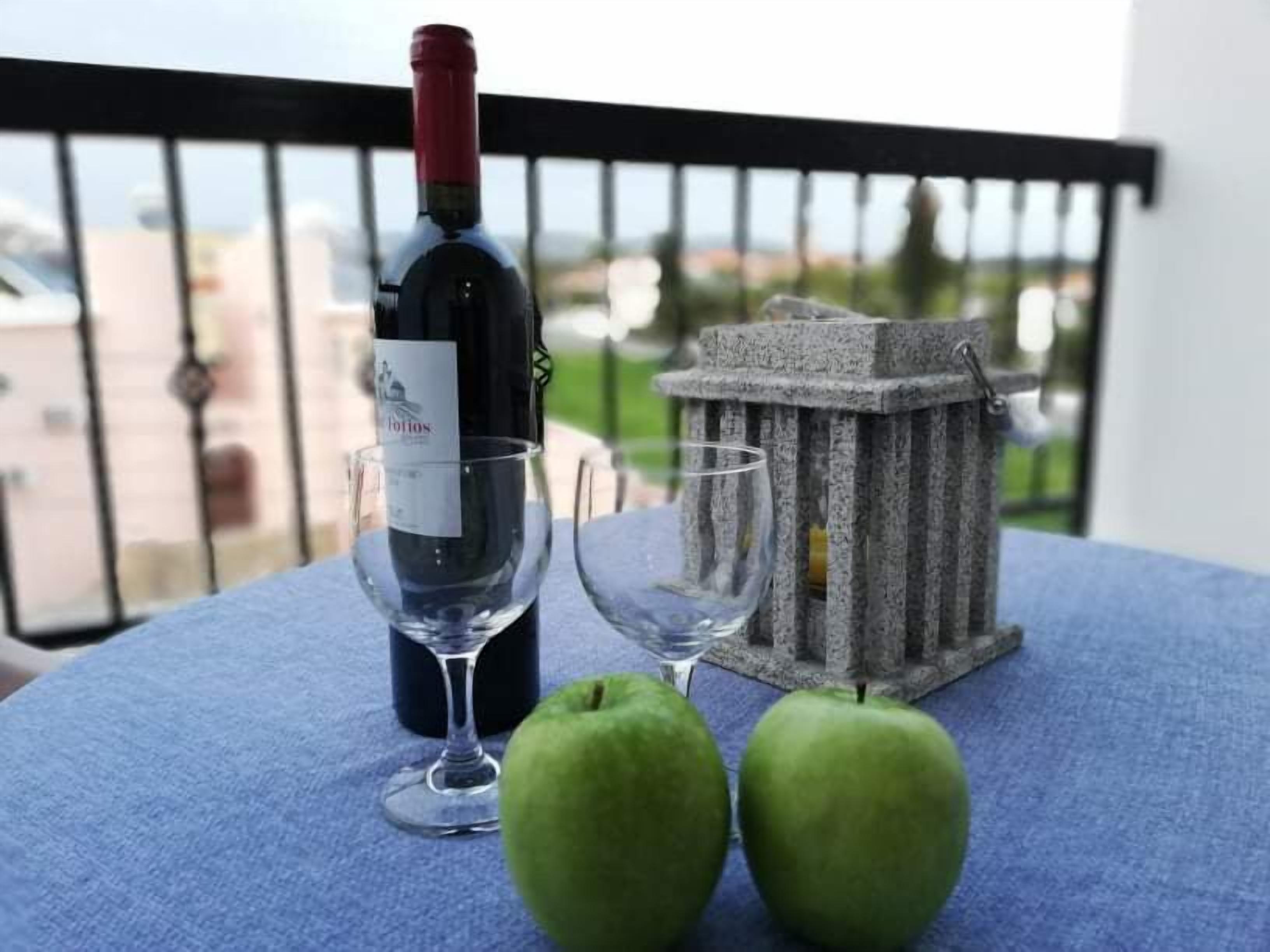 Une table avec une bouteille de vin, deux verres et deux pommes vertes sur un balcon.