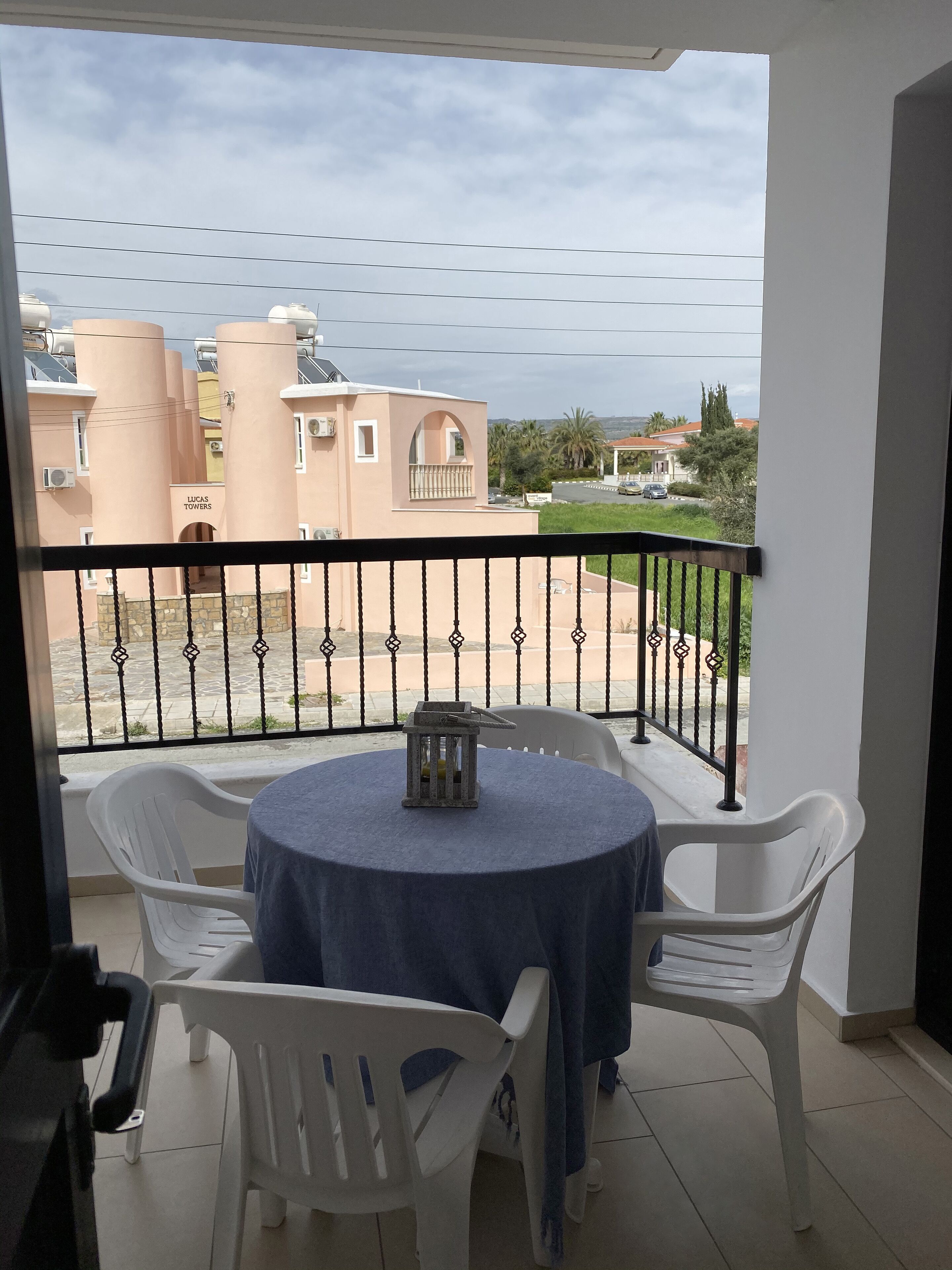 A balcony with a table and chairs, overlooking a residential area with buildings and a road.