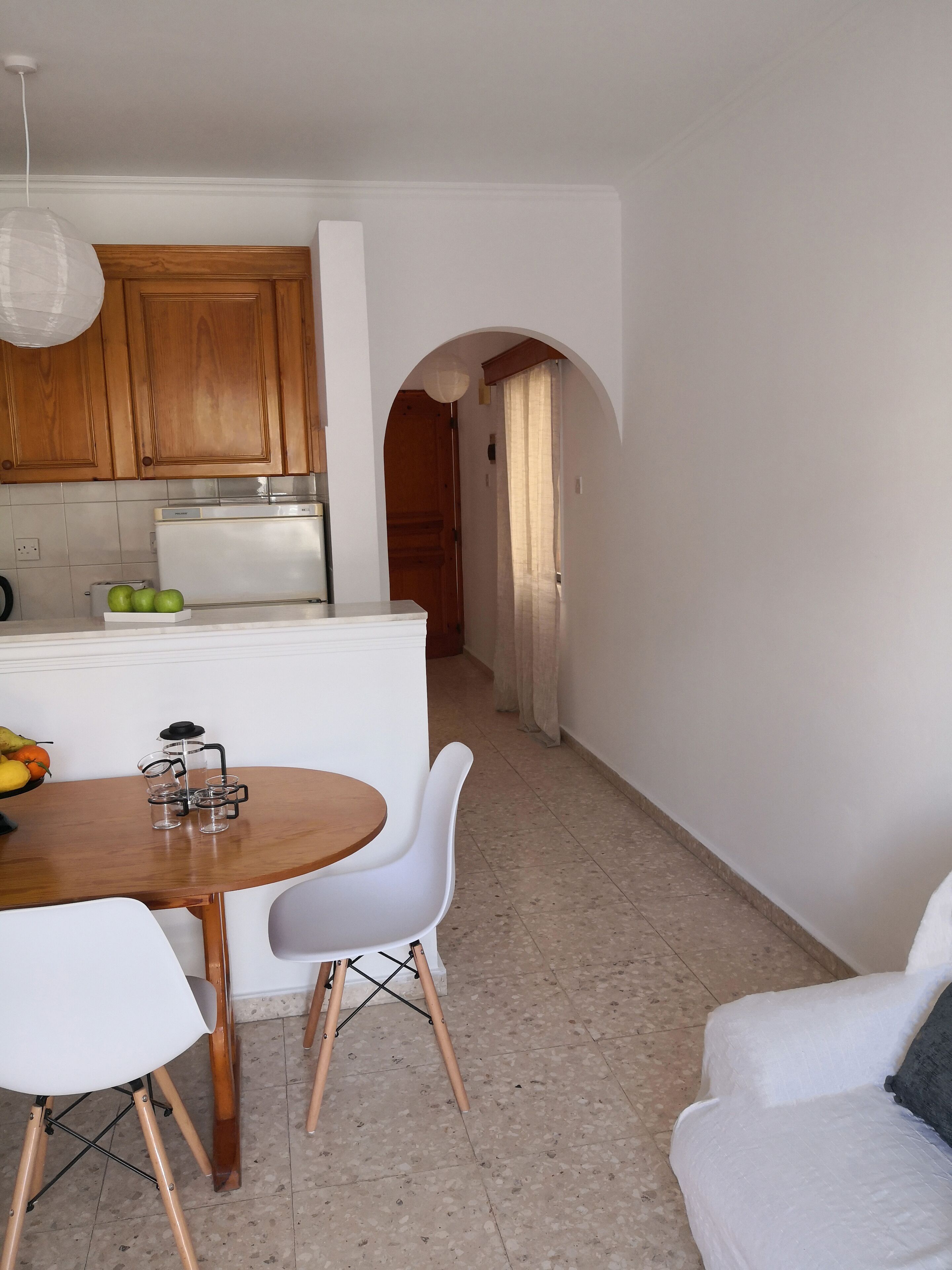 Een moderne keuken met houten kastjes, een wit aanrecht en een eethoek met een ronde tafel en witte stoelen.