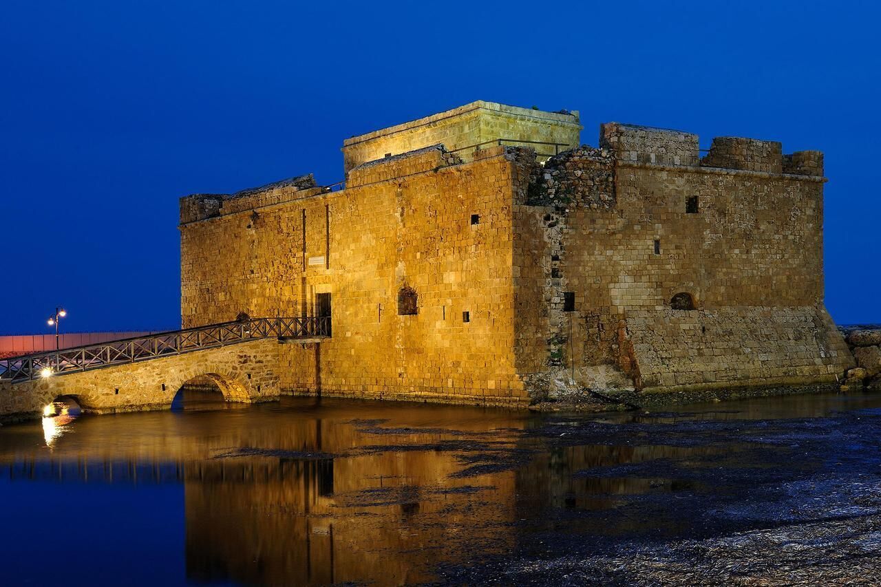 A historic stone castle with a moat, illuminated by artificial lighting.