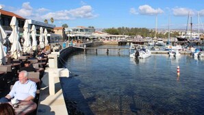 A marina with boats docked, outdoor seating with umbrellas, and a clear view of the water. - Seashell Apartments (Paphos)