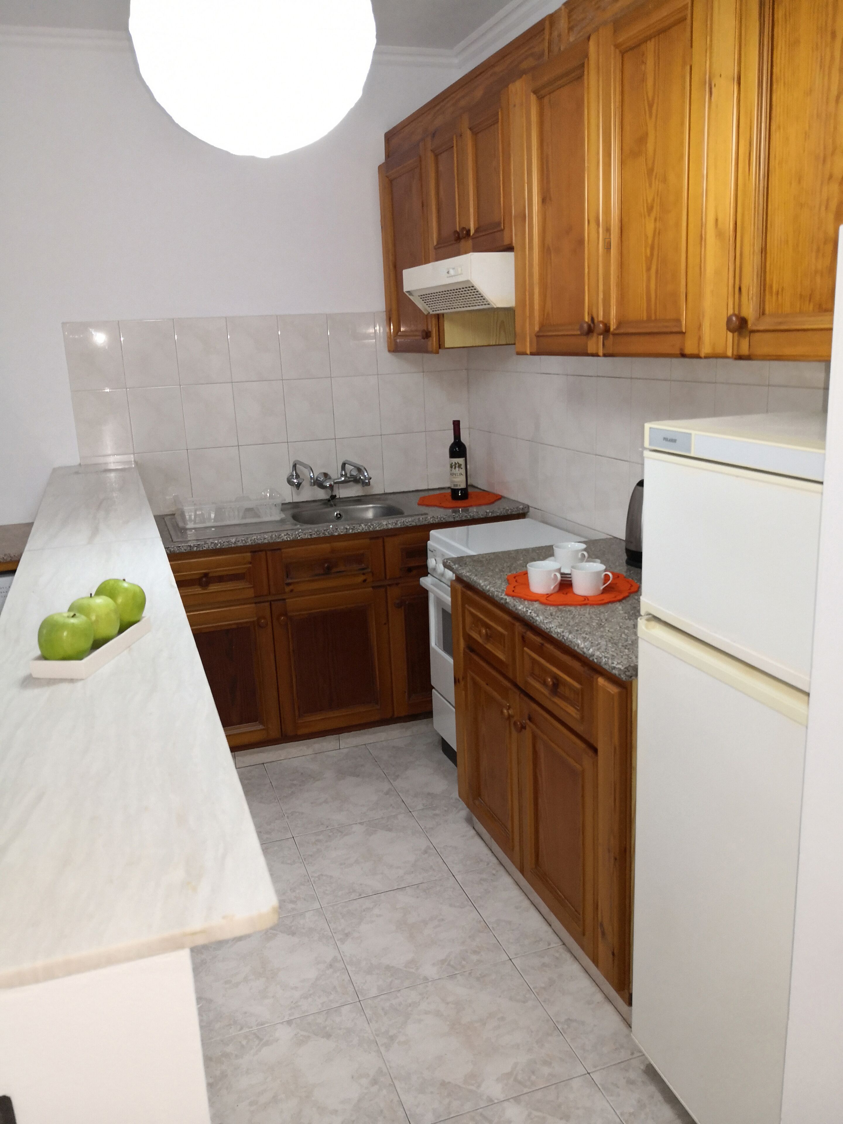 Una cocina con armarios de madera, encimera blanca, fregadero, estufa y refrigerador.
