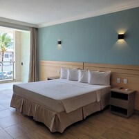 A hotel room with a large bed, a wooden headboard, two bedside tables, and a view of the outside through a glass door.