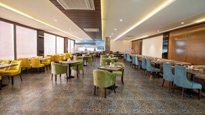 Un restaurant spacieux doté d’un sol à motifs, de chaises jaunes et vertes, et de lambris en bois sur les murs.