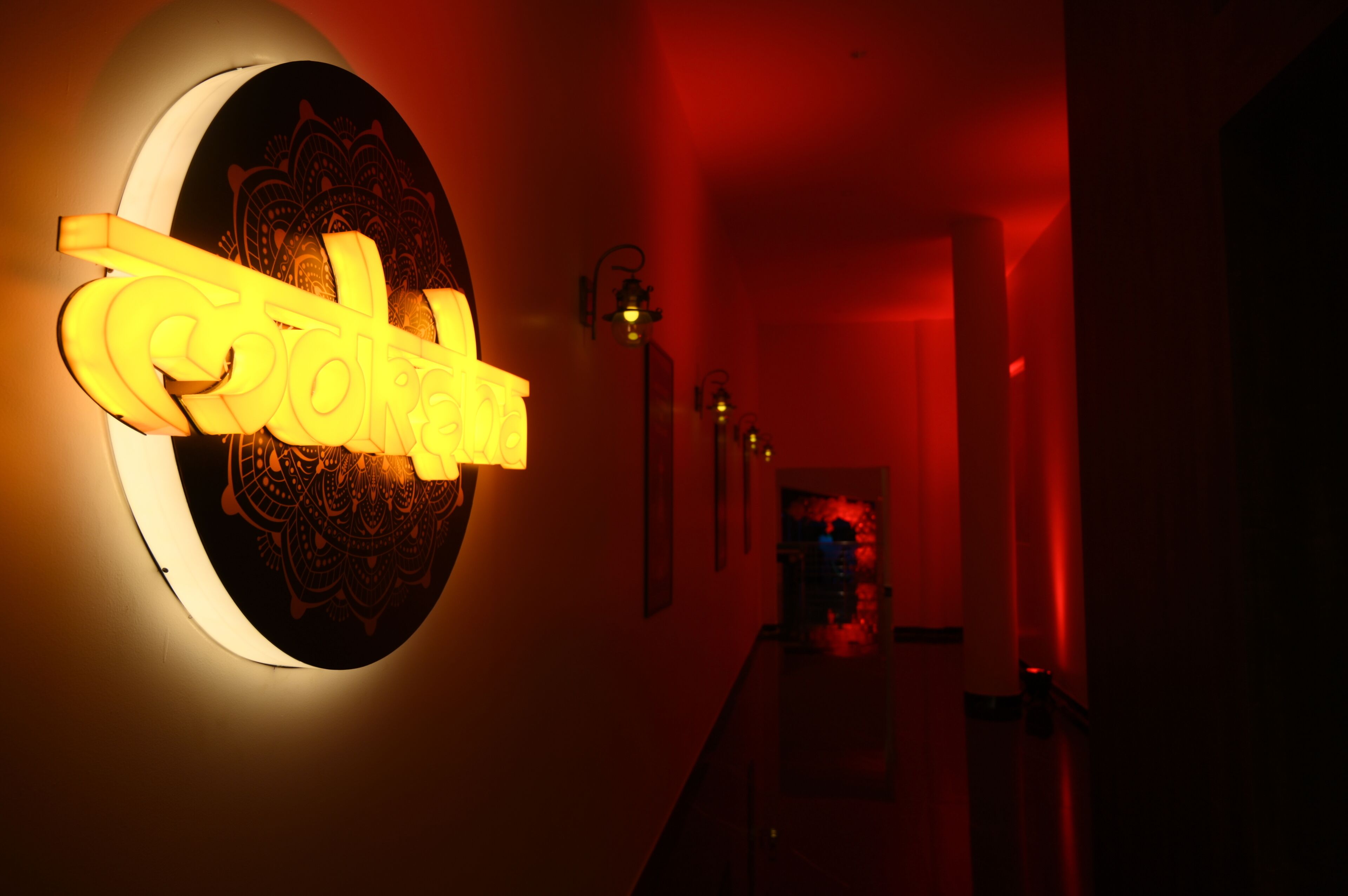 A hallway with a neon sign reading "cokah" and a circular wall decoration.