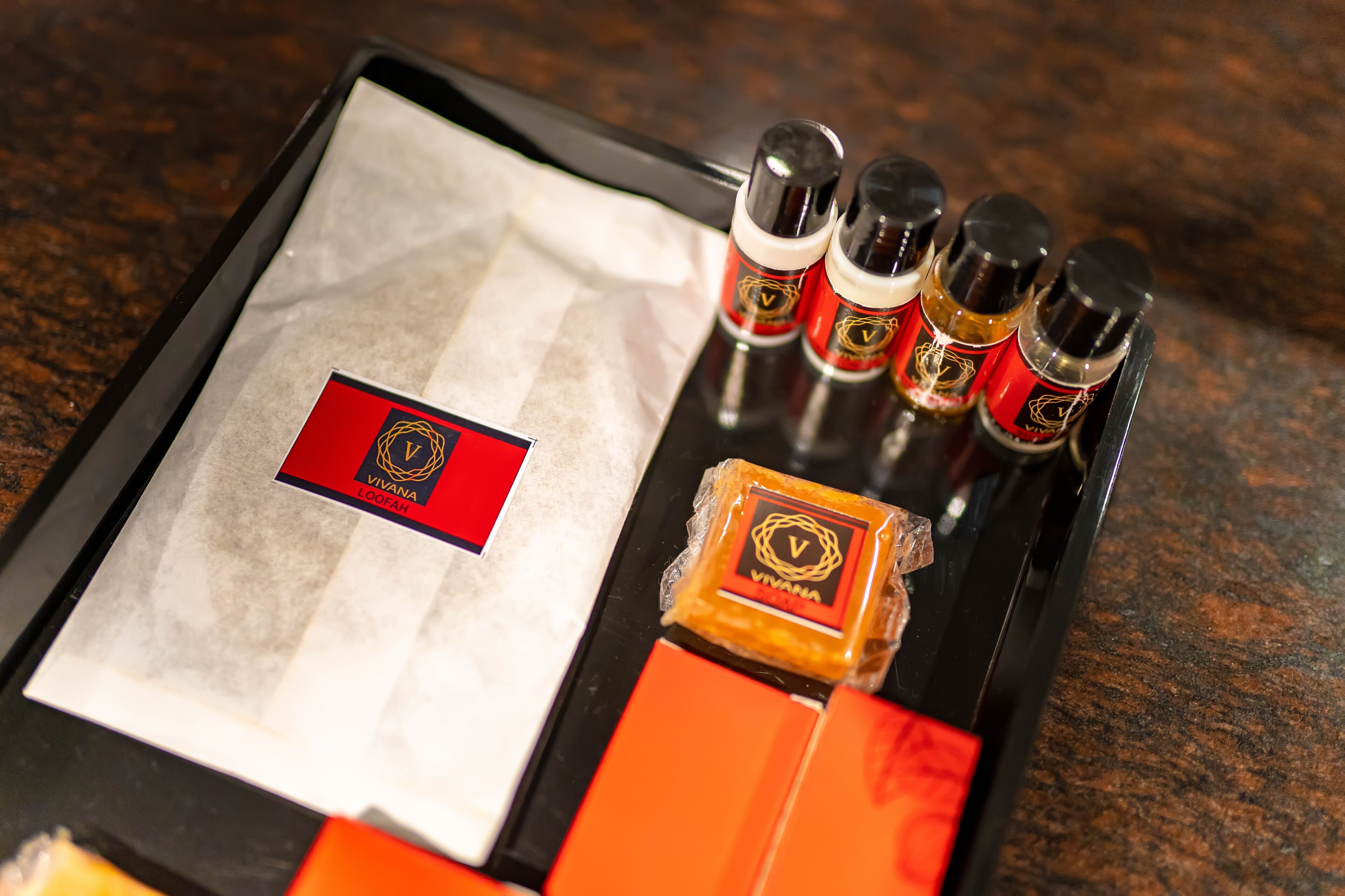 A tray with a red card, four bottles, and a small square item on a dark surface.