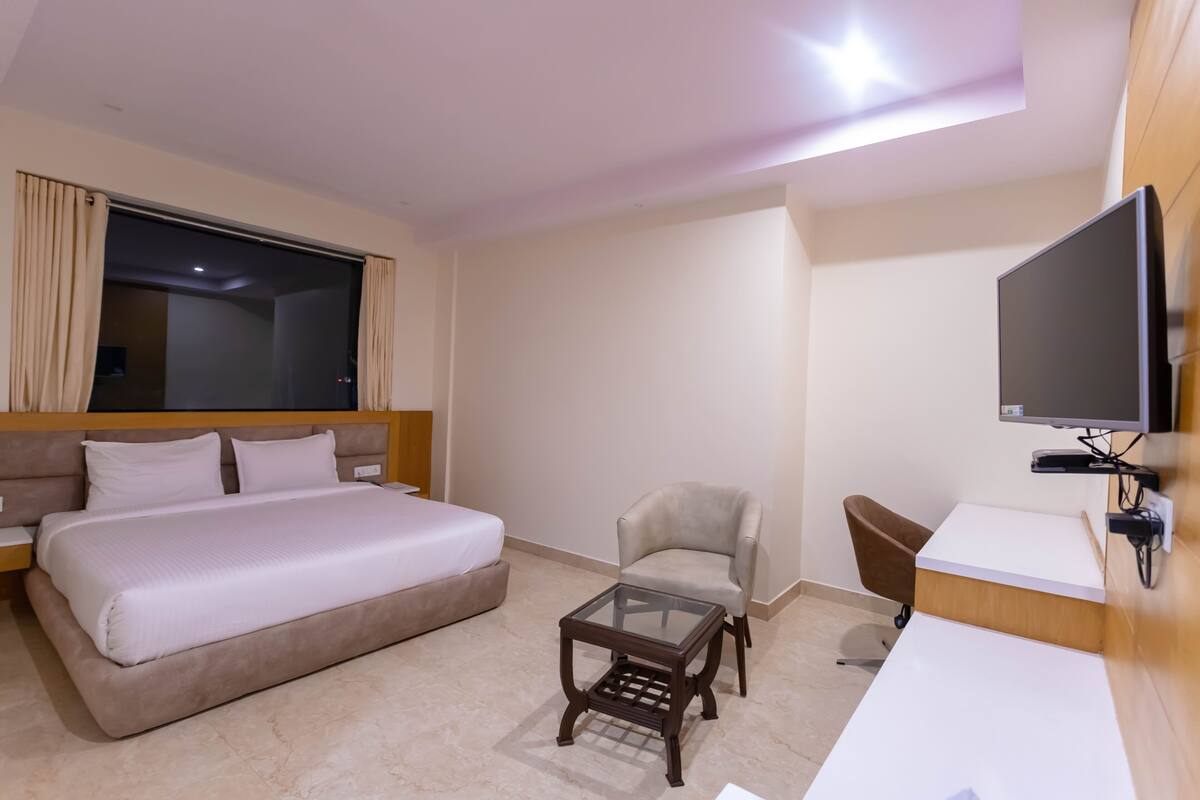 Quarto de hotel com uma cama grande, uma mesa pequena, uma cadeira, uma escrivaninha e uma televisão.