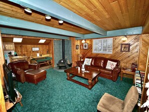 Interior acolhedor de cabana com decoração em madeira, lareira, área de jantar e sala de estar com mobiliário de couro.