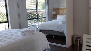 Een hotelkamer met twee bedden, een houten hoofdbord, een nachtkastje met een lamp en uitzicht door een groot raam.