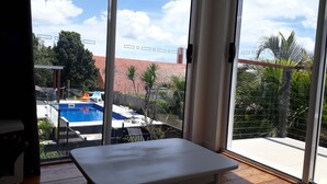 Een balkon met uitzicht op een zwembad, tuinmeubilair en een gebouw met een rood dak op de achtergrond.