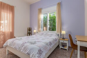 Un dormitorio con cama, escritorio, silla, lámpara y ventana con cortinas.