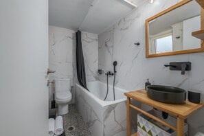 Moderni kylpyhuone, jossa on valkoinen kylpyamme, wc-istuin ja pesuallas, jonka yläpuolella on peili.