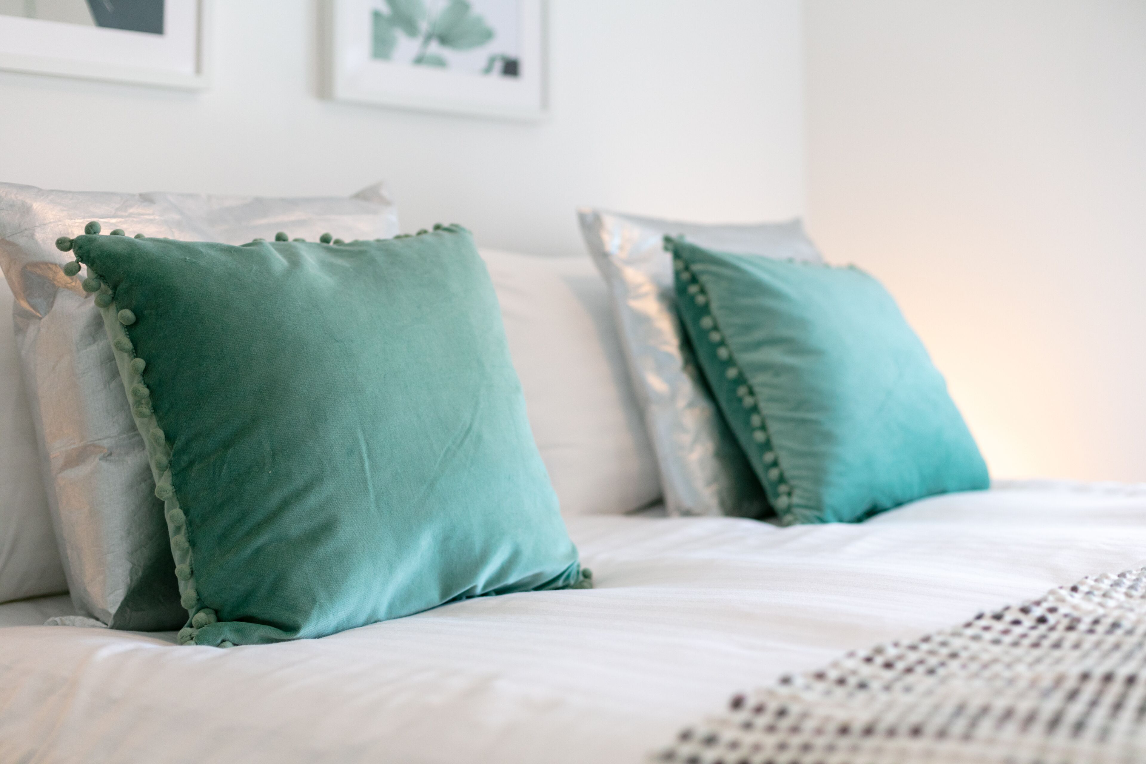 A neatly made bed with teal pillows and a white bedspread.