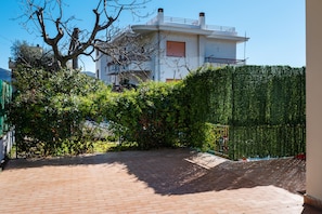 A courtyard with a paved area, a white building with balconies, and dense green foliage.