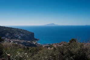 A coastal town with buildings along the cliffside, a clear view of the sea, and a distant mountain.