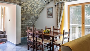 Un comedor con techo de piedra, mesa y sillas de madera, un cuadro en la pared y vistas a través de un ventanal.