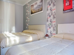 Un dormitorio con dos camas, una mesita de noche, una lámpara y una ventana.