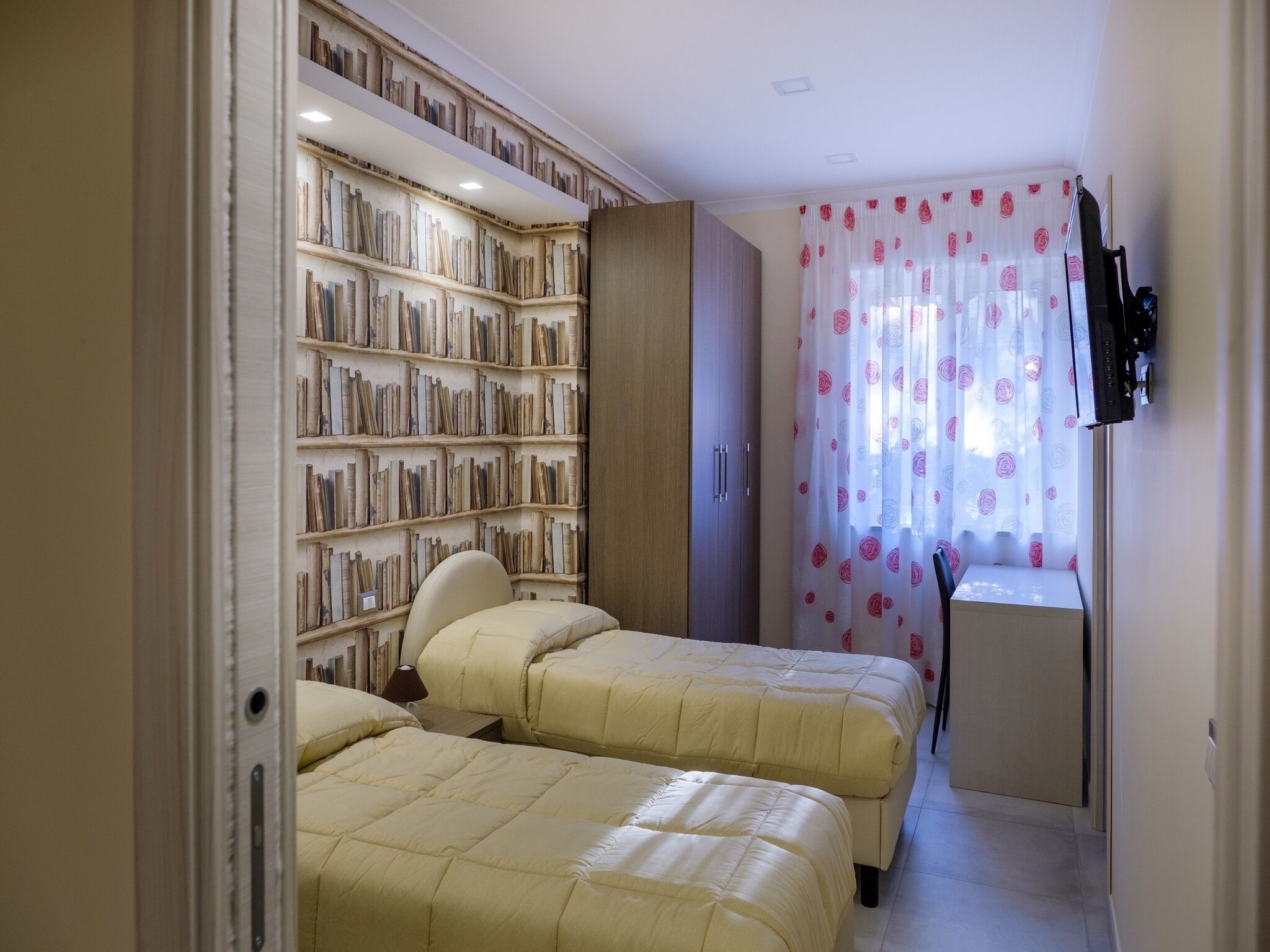 Un dormitorio con dos camas, una estantería, un escritorio y un televisor.