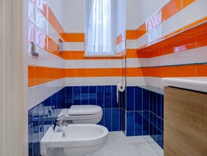 A bathroom with a toilet, bidet, and sink, featuring orange and blue tiles. - Casa Micla (Vico Equense)