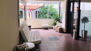 A spacious living area with a sofa, a small round table, and a large window offering a view of greenery and a tiled roof outside. - SimOtel Ermis (Kassandra)