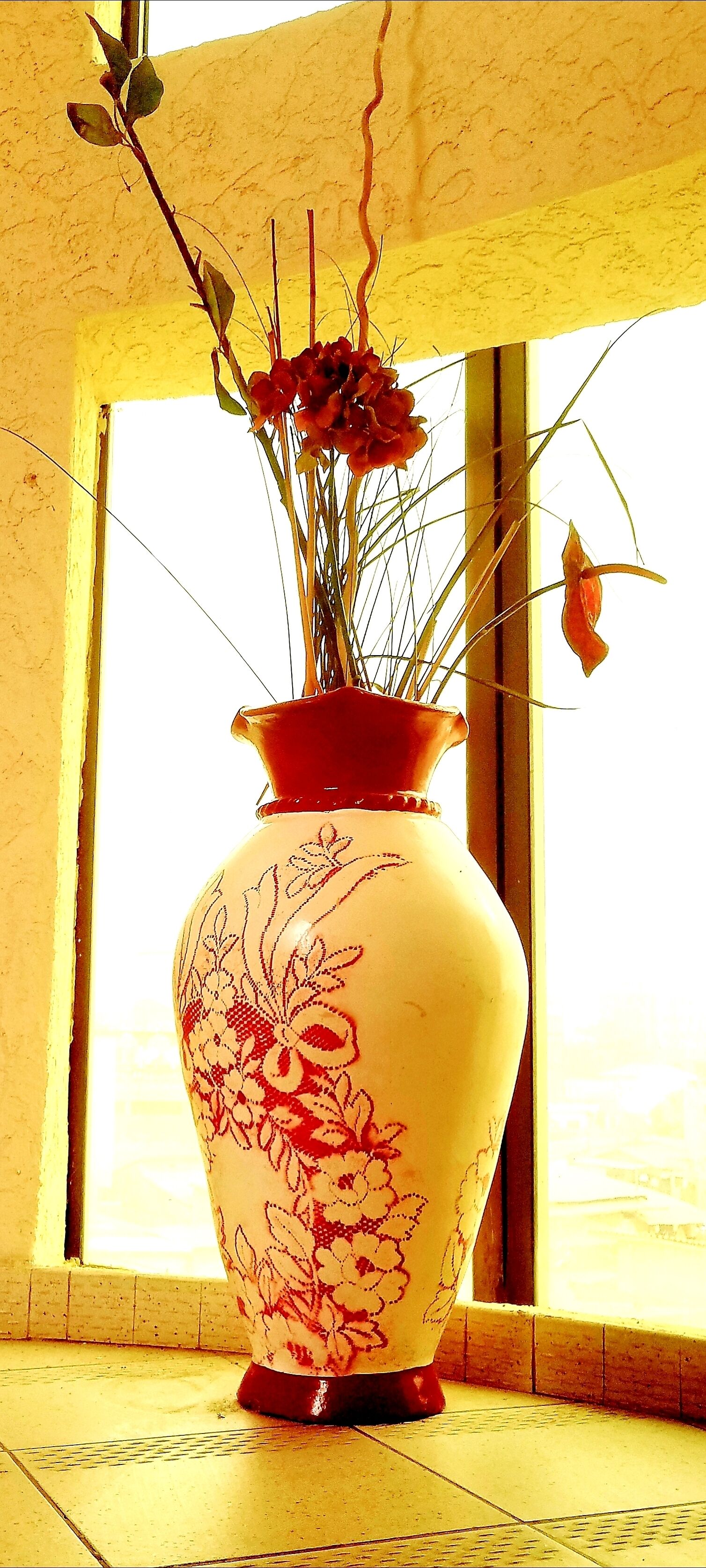A large vase with floral patterns on a tiled floor near a window.