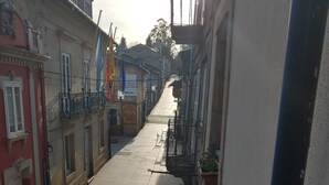 A narrow street with buildings on either side, featuring balconies with railings and potted plants. - El Bordón de la Casa Batallón (Sarria)