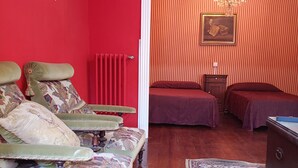 A room with a red wall, a patterned sofa, a wooden floor, a patterned rug, and a bed with a red bedspread. - El Bordón de la Casa Batallón (Sarria)