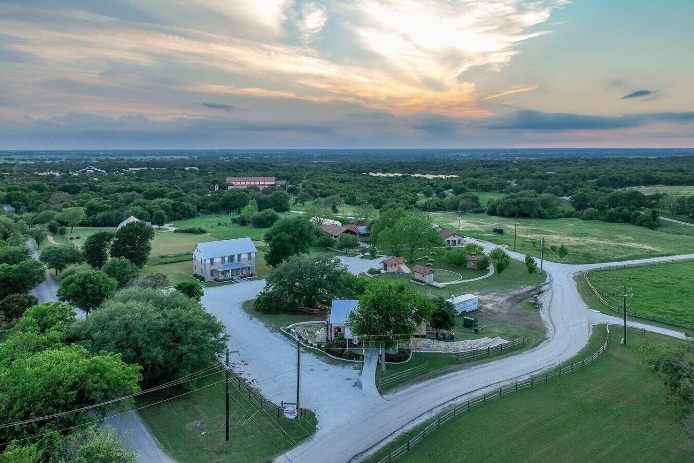 A rural landscape with a winding road, a large white building, and surrounding greenery.