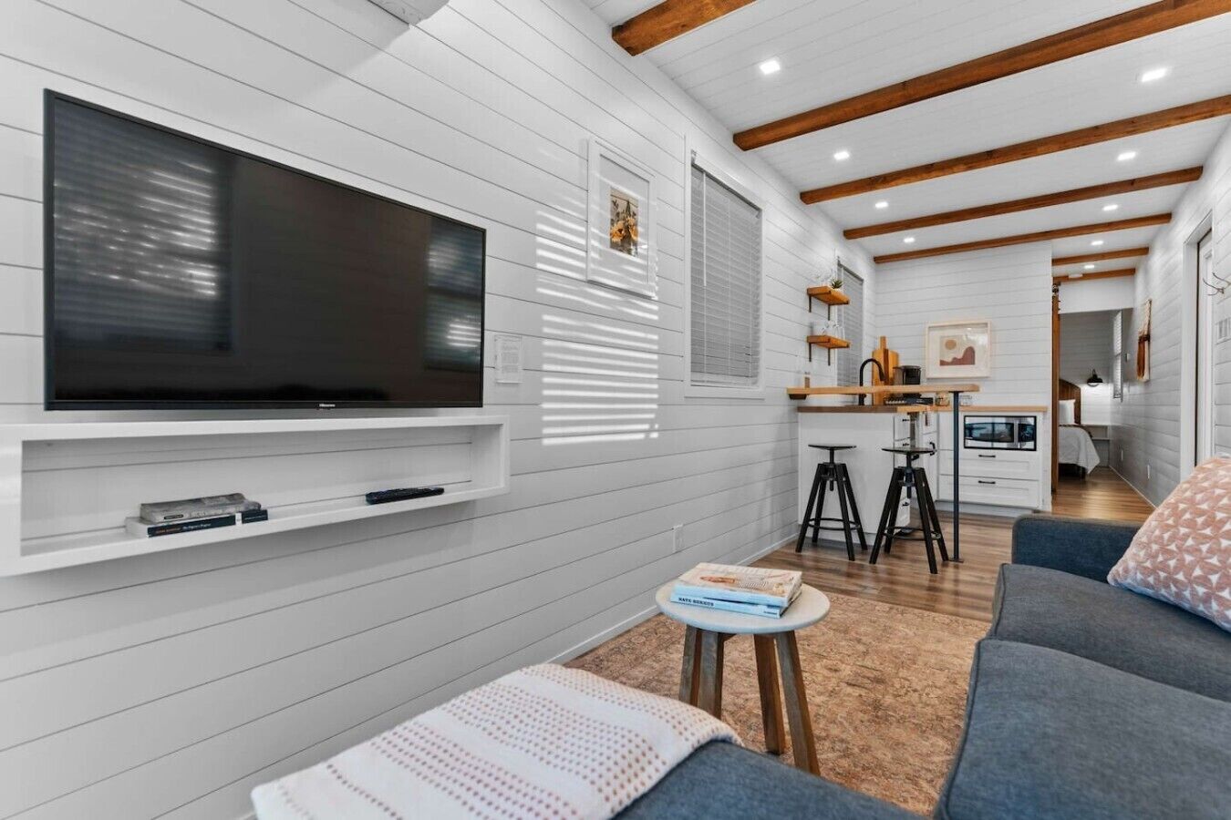 Una sala de estar moderna con una televisión de pantalla plana, un sofá, una mesa de centro y una zona de cocina con taburetes.