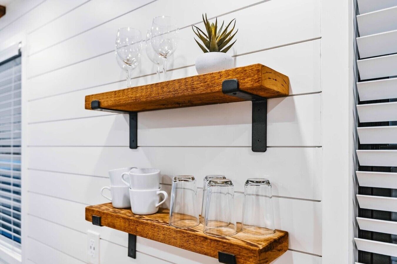 Two wooden wall shelves with glassware and a small plant.