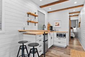 A compact kitchen with white cabinetry, wooden countertops, and a built-in oven. There are two stools and a small bar area.