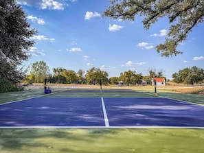 A tennis court with a net, surrounded by trees and a building in the background.