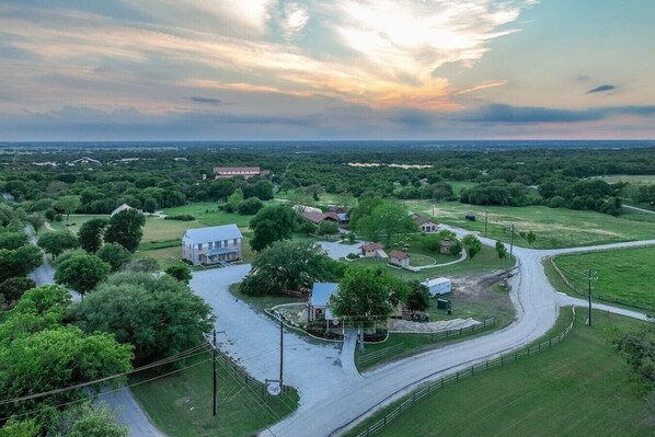 A rural landscape with a winding road, a large white building, and surrounding greenery.