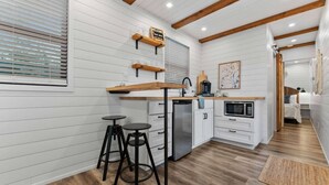 Une cuisine compacte avec un lambris blanc, des poutres en bois, un four à micro-ondes encastré et un petit coin repas avec des tabourets.