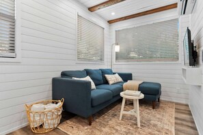 Ein Zimmer mit einem blauen Sofa, einem kleinen runden Tisch, einem Korbwäschesessel und Holzboden.