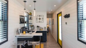 A modern kitchen with pendant lighting, a built-in microwave, and a large window. - Tiny Container Home with Rooftop Deck (Waco)