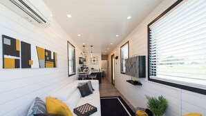 A modern living room with a sofa, a coffee table, and a TV mounted on the wall. - Tiny Container Home with Rooftop Deck (Waco)