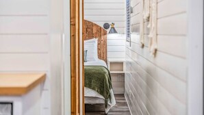 A narrow hallway leading to a bedroom with a bed, a nightstand, and a lamp. - Container home with rooftop views and pickleball (Waco)