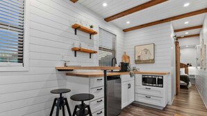 A compact kitchen with white cabinetry, wooden beams, a built-in oven, and two stools. - Container home with rooftop views and pickleball (Waco)