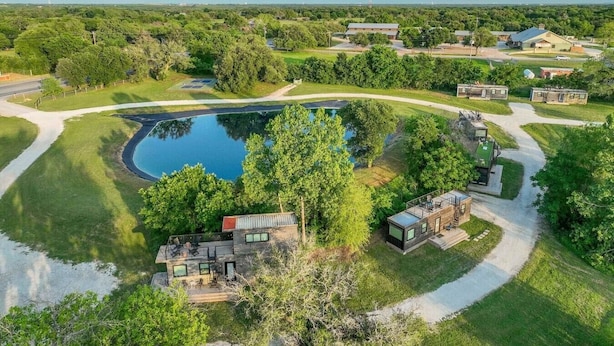 A residential area with a large pond, modern houses, and a well-maintained lawn. - Container home with rooftop views and pickleball (Waco)
