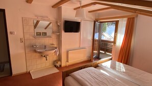 Ein Schlafzimmer mit Bett, einem Fenster mit Vorhängen, einem Heizkörper, einem Waschbecken und einem Spiegel.