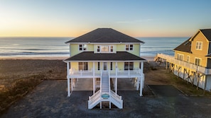 Uma casa de praia de dois andares com varanda e pequeno alpendre, próxima ao oceano.