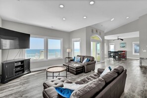 A spacious living room with a large sectional sofa, a flat-screen TV, and a dining area with a table and chairs. - Oceanfront Home, Private Beach Access, sunrise views, pet friendly (North Topsail Beach)