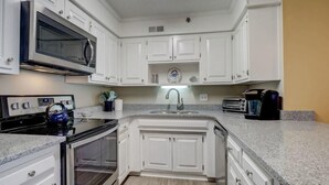 A modern kitchen with white cabinetry, a microwave, a kettle, a toaster, and a sink. - Amazing views of the ocean, community pool, private covered deck (North Topsail Beach)