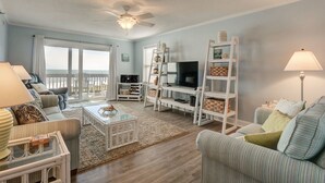 A spacious living room with a large TV, comfortable seating, a ceiling fan, and a view of the ocean. - Amazing views of the ocean, community pool, private covered deck (North Topsail Beach)