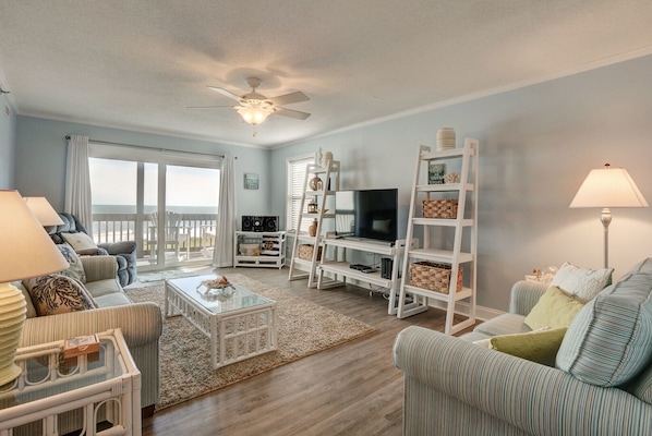 A spacious living room with a large TV, comfortable seating, a ceiling fan, and a view of the ocean. - Amazing views of the ocean, community pool, private covered deck (North Topsail Beach)