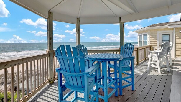 A covered outdoor area with a view of the ocean, featuring a table and blue chairs. - 8 Bedroom Direct Oceanfront Home, Private Pool, Media Room, Private Beach Access, 2025 Updates (North Topsail Beach)