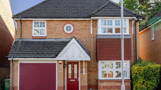 A two-story residential building with a red garage door, a front door, and a small porch. - Modern 4 Bedroom Detached House in Cardiff (Cardiff)