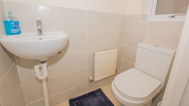A bathroom with a white sink, a toilet, and a window. - Modern 4 Bedroom Detached House in Cardiff (Cardiff)