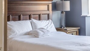 A neatly made bed with white linens and pillows, a wooden headboard, a bedside table with a lamp, and a nightstand with a drawer. - Modern 4 Bedroom Detached House in Cardiff (Cardiff)